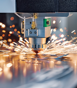 A machine cutting metal with sparks, while fire safety equipment is present nearby.